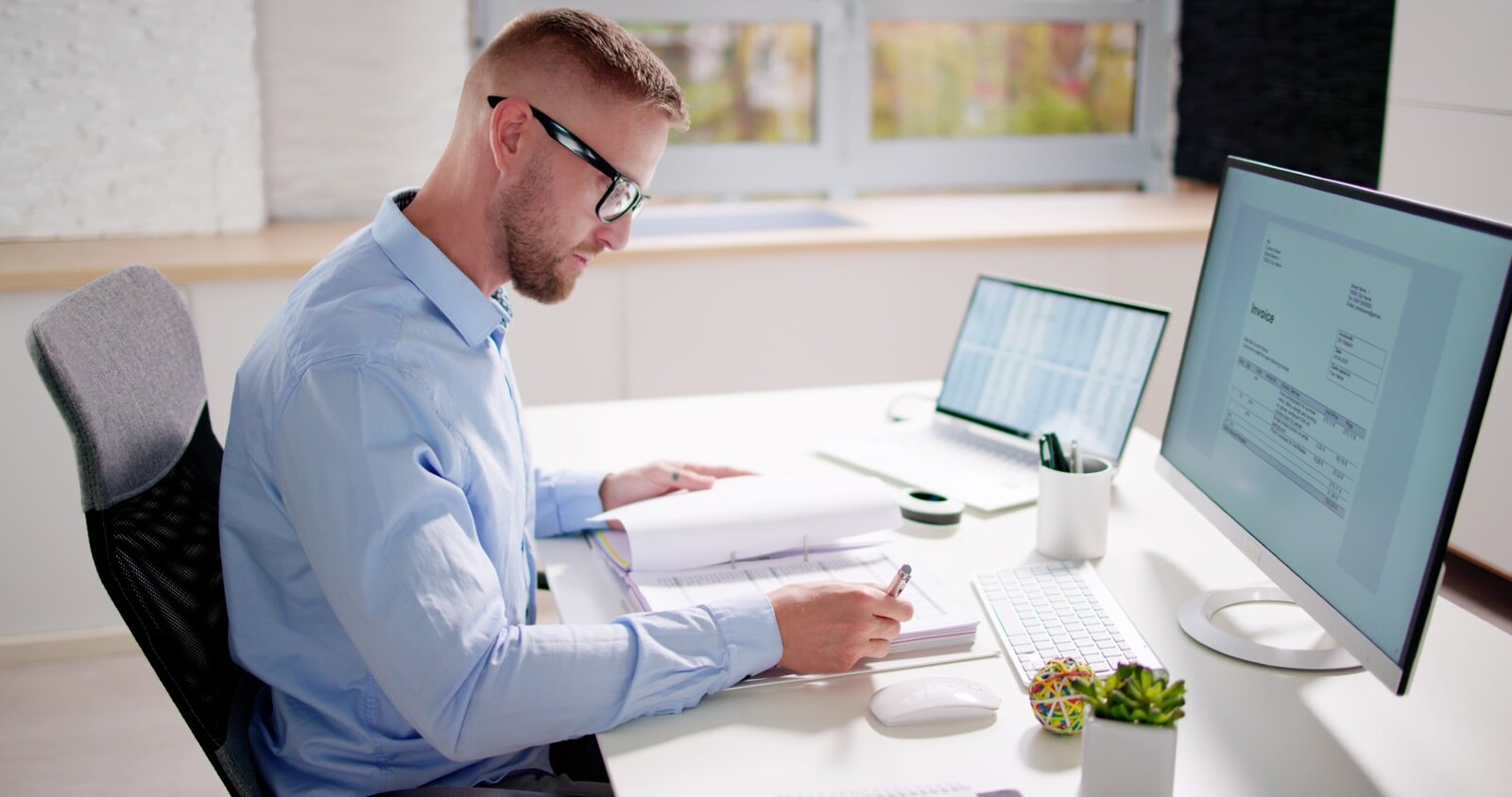 Mann am Laptop mit Rechnungspapieren auf Schreibtisch